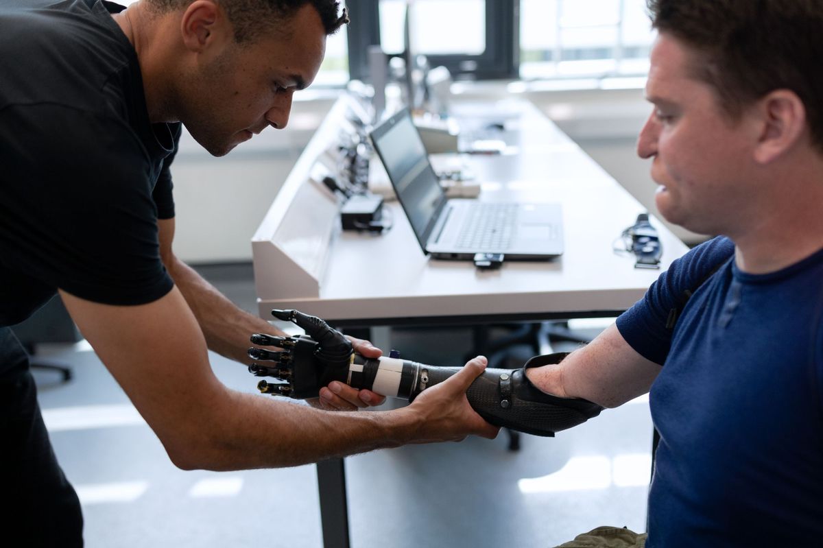 Engineer leaning in to adjust a carbon-fibre bionic hand with a laptop and components behind