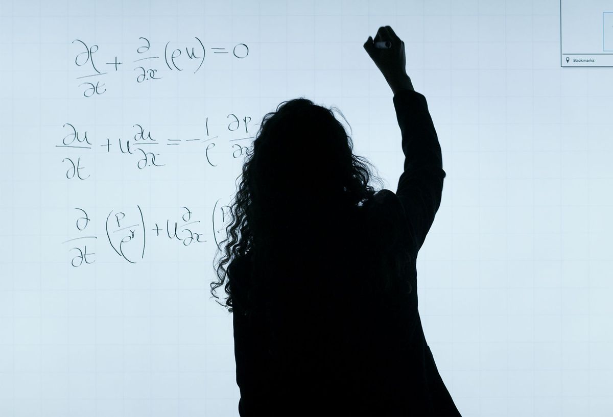 Silhouette of a researcher writing partial differential equations on a backlit glass board