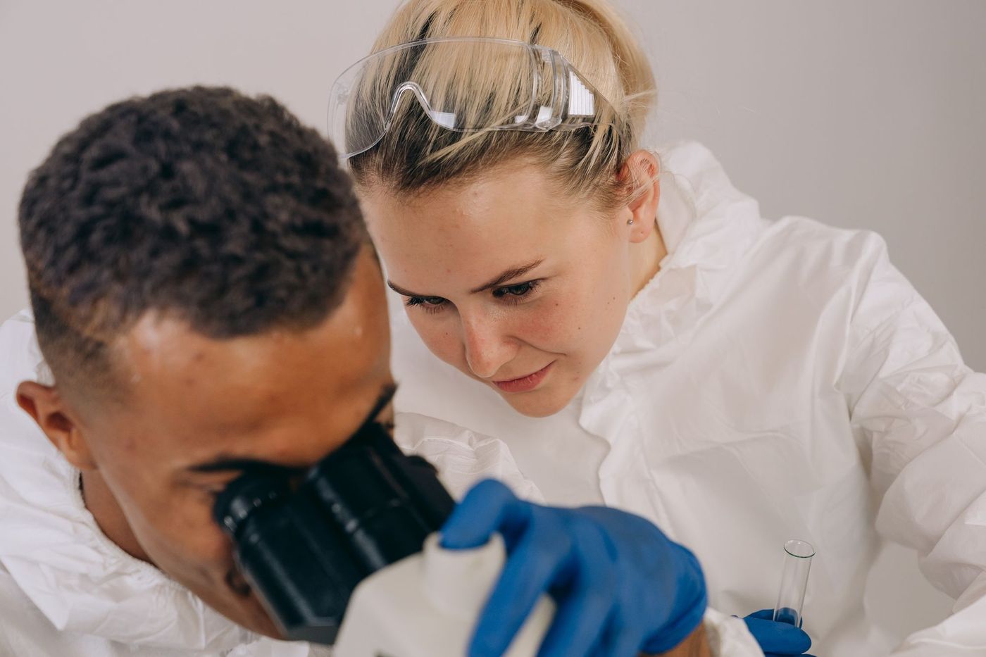 Two researchers in safety goggles examining a sample together at a microscope