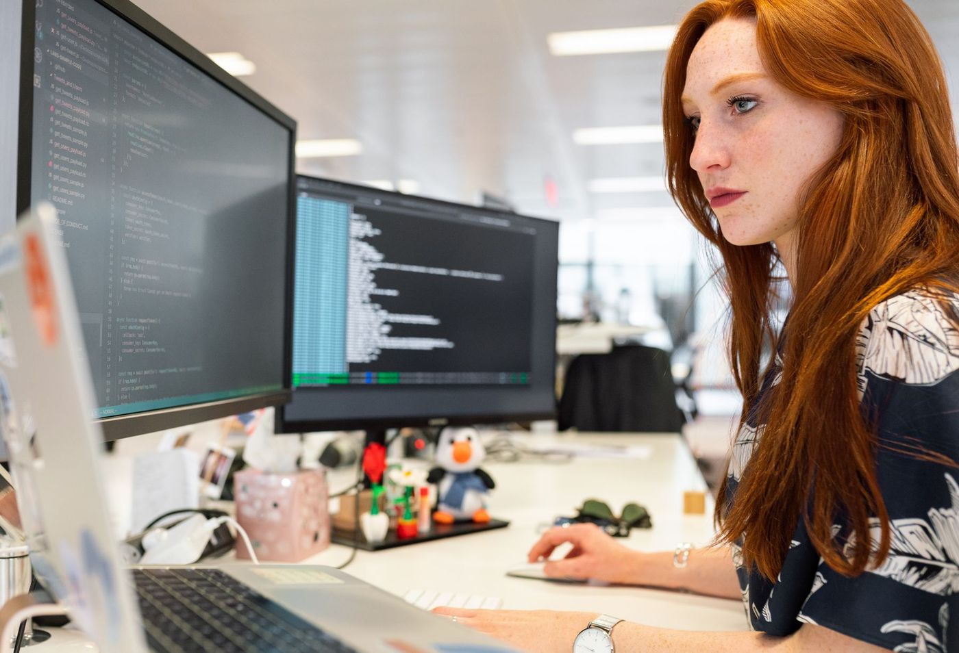 Engineer concentrating on code across two monitors in a bright open-plan office