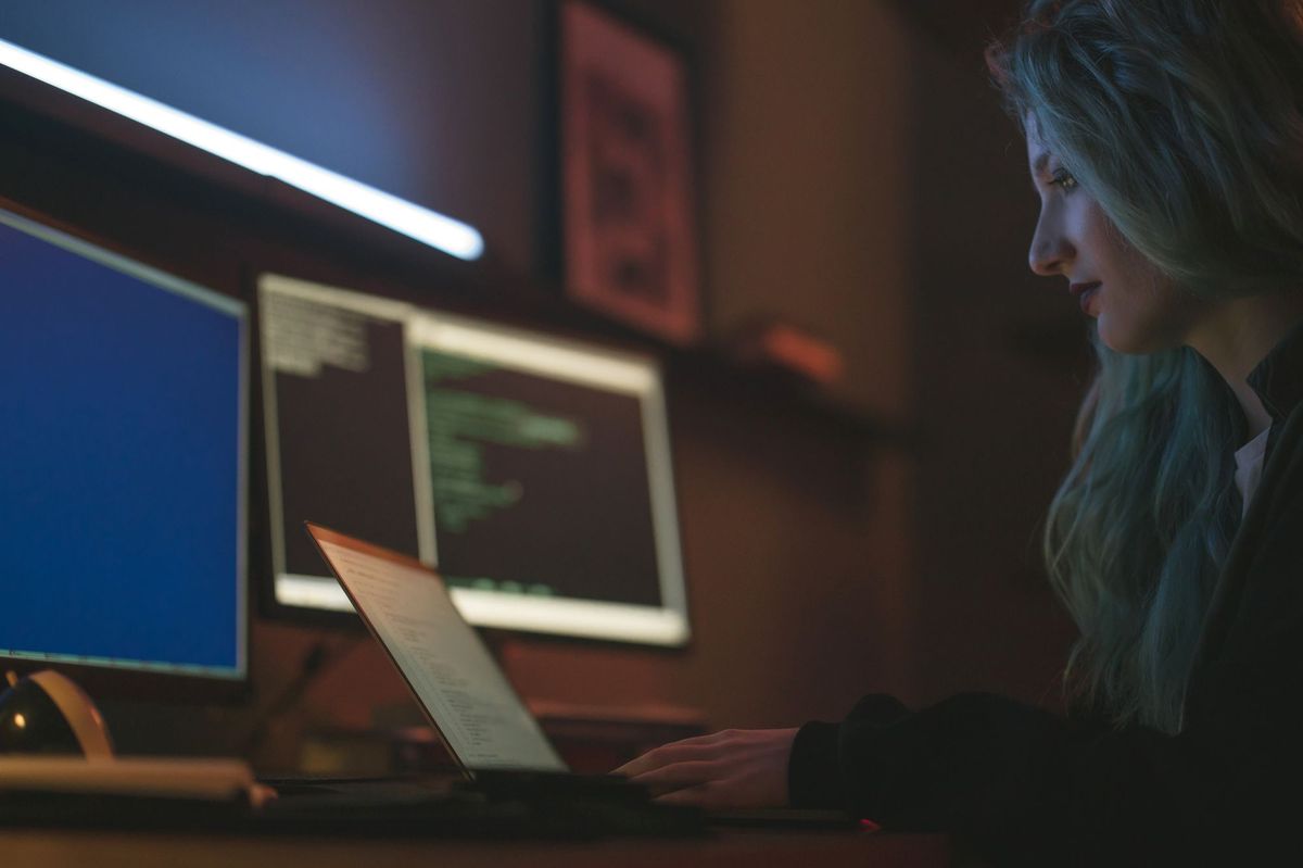 Engineer lit by monitor glow working across three terminal screens in a dark room